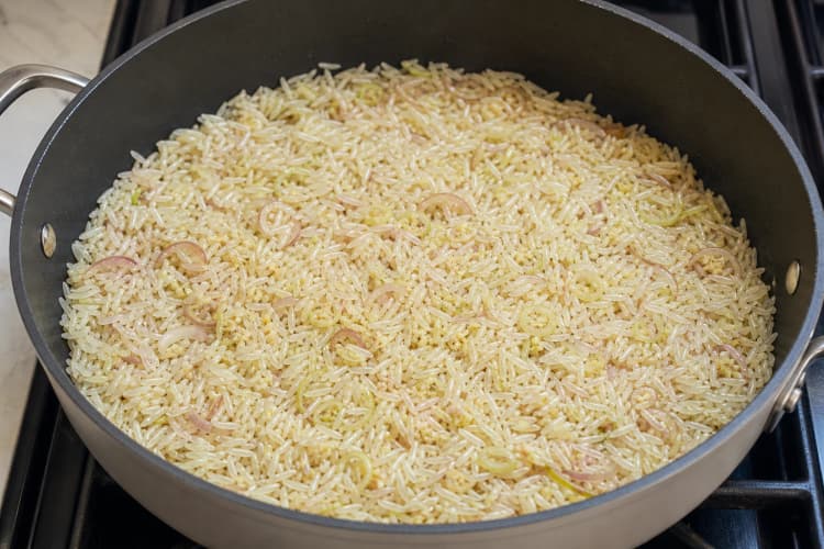 One-Pan Chicken and Crispy Rice method step 3, Build a fat-toasted rice base: Aromatic pieces are pale gold, rice tips look translucent, and no wet clumps remain.
