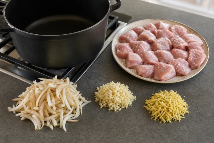 One-Pot Chicken Curry method step 1, Season the chicken and stage the aromatics: Chicken surfaces look matte rather than wet, pieces are even, and three separate aromatic piles are ready beside the hot pot.