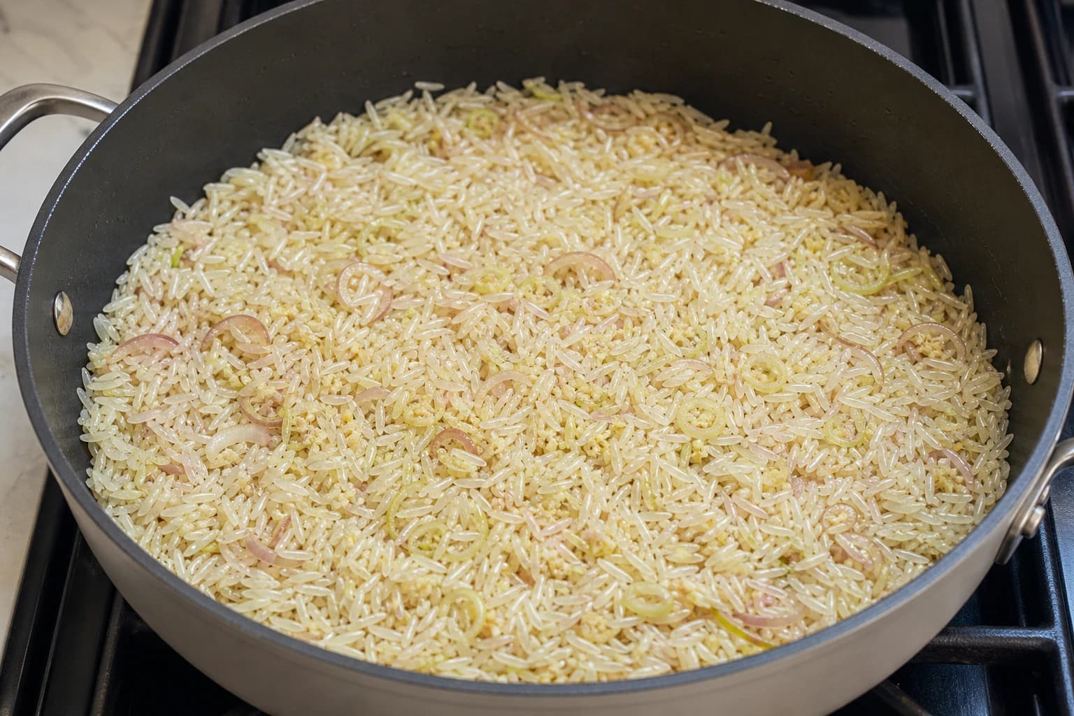One-Pan Chicken and Crispy Rice, step 3, Build a fat-toasted rice base: Aromatic pieces are pale gold, rice tips look translucent, and no wet clumps remain.