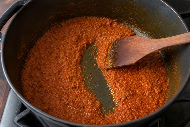 Penang Nyonya Kari Kapitan method step 3, Fry the rempah past its raw steam: The rempah is deep orange-red, roughly half its initial volume, and a spatula trail remains open while clear oil glints at the edges.