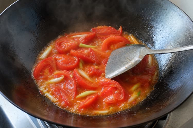 Tomato Egg Stir-Fry method step 4, Draw a fresh sauce from the tomatoes: Wedge edges soften and release an orange-red sauce that coats the wok while most centres remain intact.