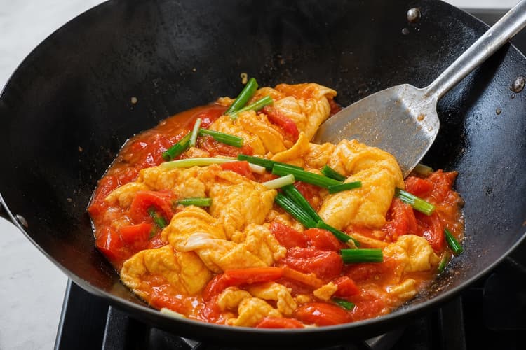 Tomato Egg Stir-Fry method step 5, Fold once, verify, and serve: Distinct golden folds hold red-orange sauce in their creases, with bright scallion and no watery pool.