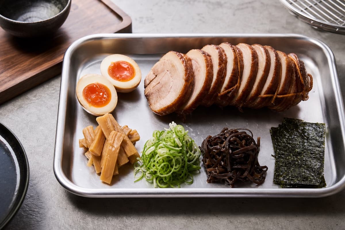 Tonkotsu Shoyu Ramen, step 6, Cook ajitama and stage every topping: Egg whites are fully set around custardy amber yolks; chashu rounds are intact and every cold topping has its own measured service container.